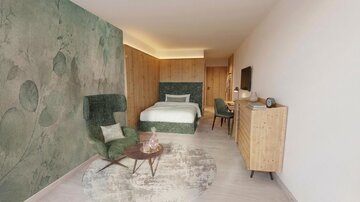 A modern room with a bed and a comfortable seating area. The walls are painted in soft green tones, and the furniture is made of light wood.
