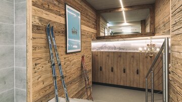 A cozy entrance area with wooden paneling and skis. In the background, there are cabinets and modern lighting visible.