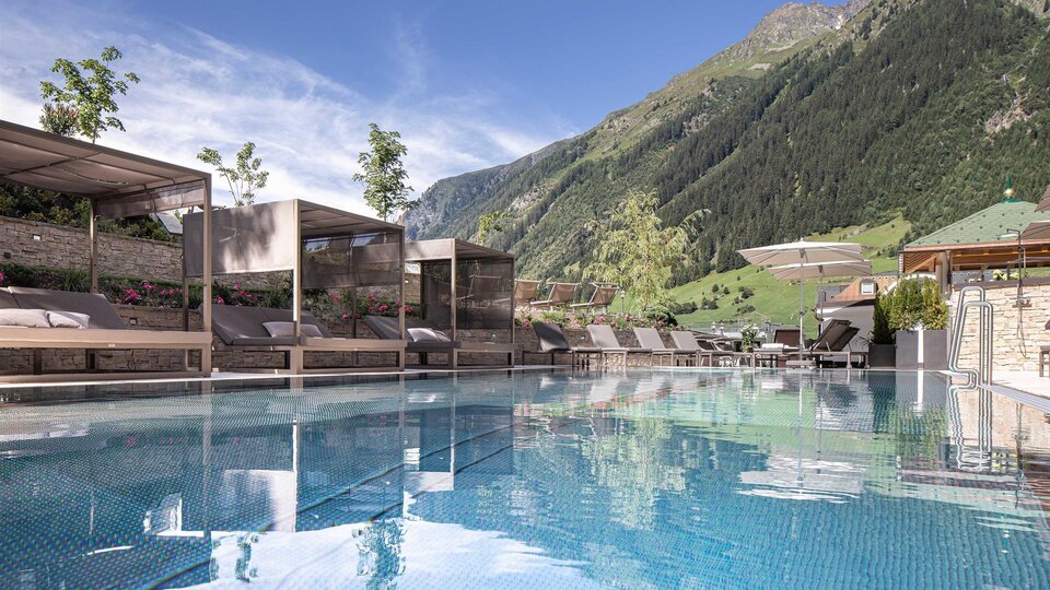A beautiful pool with a view of the mountains and a clear, blue sky. Loungers and shaded areas invite you to relax.