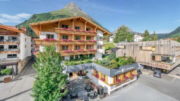 A charming mountain village with traditional wooden houses and a picturesque landscape. In the foreground, cozy terraces and green spaces can be seen. | © Rössle