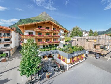 A charming mountain village with traditional wooden houses and a picturesque landscape. In the foreground, cozy terraces and green spaces can be seen. | © Rössle