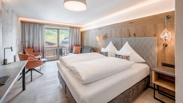 A modern hotel room with two beds, a cozy seating area, and a view of nature. The warm wooden paneling creates an inviting atmosphere.