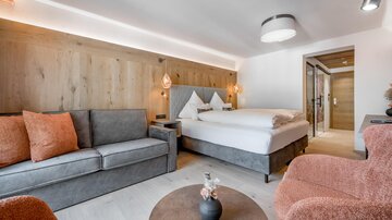 A modern room with a large bed and comfortable seating. The warm colors and wooden details create an inviting atmosphere.
