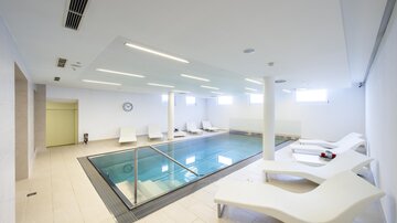 A modern indoor swimming pool with crystal clear water and comfortable loungers. The room is bright and designed in a minimalist style. | © Rössle