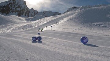 A snowy mountain landscape with skiers on the slope. In the foreground, there are blue balls that are part of the ski area.