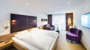 A modern hotel room with a double bed and a cozy sofa. Large windows provide plenty of daylight and a pleasant atmosphere. | © Rössle