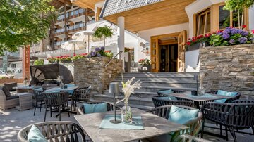 An inviting terrace with stylish chairs and tables.  
Blooming plants and a sunny atmosphere create a cozy ambiance. | © Rössle