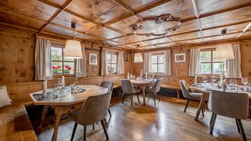 A cozy restaurant with wood paneling and warm lighting. The tables are beautifully set and offer space for several guests. | © Rössle