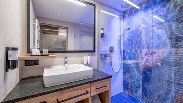A modern bathroom with a glass shower and an elegant sink. The wall in the background features an artistic, colorful design.