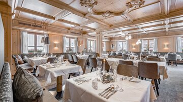 An elegant restaurant with stylish tables and chairs. The ceiling is artistically decorated and the atmosphere is cozy.