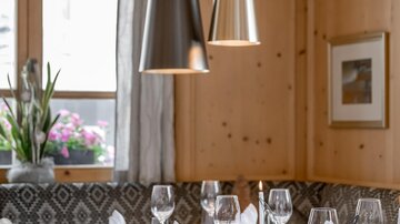 An elegant restaurant with a beautifully set table. The walls are made of light wood, and stylish lamps hang from the ceiling.