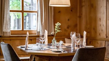 An inviting table in a cozy restaurant. It is set with glasses, cutlery, and a small floral decoration.
