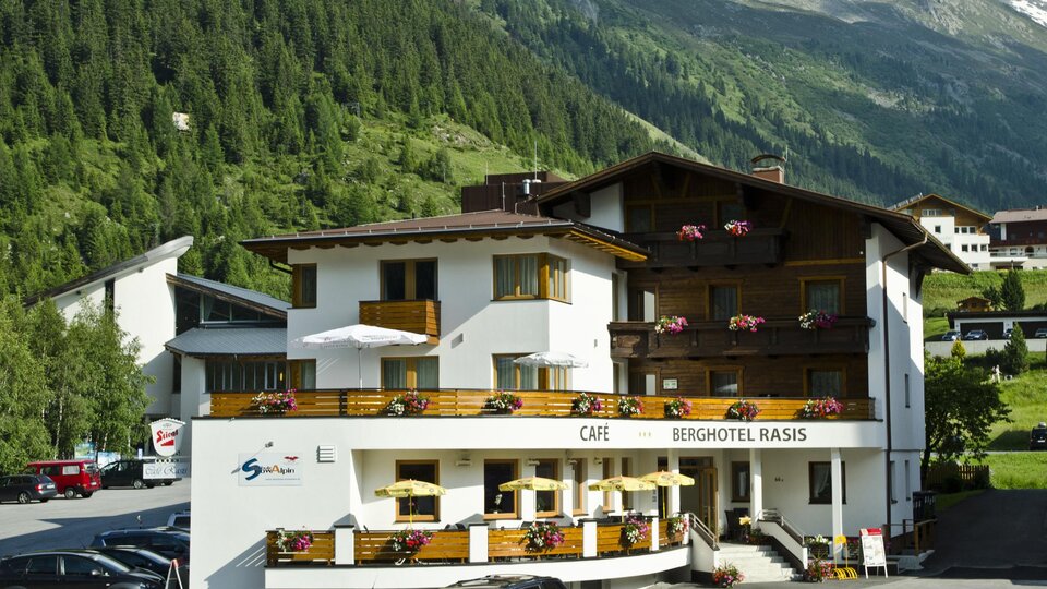A charming mountain hotel with outdoor seating and beautiful balconies.  
Surrounded by green forests and majestic mountains.