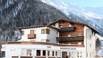 A charming mountain hotel with a café, surrounded by snow-capped mountains. The clear winter landscape creates an inviting atmosphere.