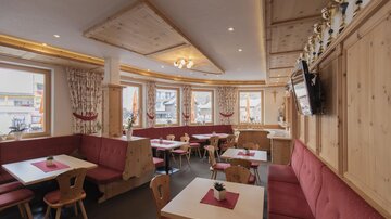 A cozy restaurant with wooden paneling and red seats. The windows offer a view outside and there are tables for guests.