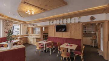 A cozy restaurant with wooden decor and red upholstered furniture. There are tables with chairs and a bar in the background.