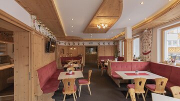 A cozy restaurant with wooden decor and red upholstered benches. The tables are simply set, and there is a warm, inviting atmosphere.
