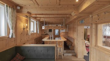 A cozy restaurant with wood-paneled walls and warm light. There are seating options and a long table in the middle.