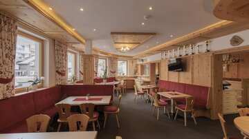 A cozy restaurant with wooden elements and red upholstered benches. Large windows provide plenty of daylight.