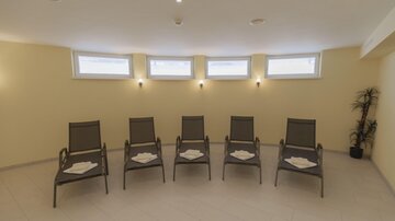 A relaxing room with five loungers and a light, warm color tone. Large windows provide natural light.