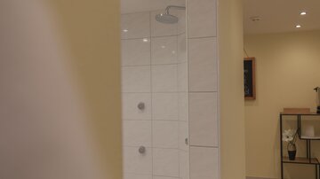 A modern shower with white tiles in a yellow room. Decorative elements and soft lighting can be seen in the background.