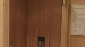 A cozy wooden sauna with a bench and a heating device. The walls are simple, light wooden panels.