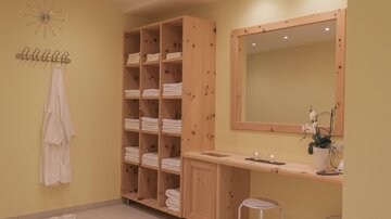 A relaxing wellness area with yellow walls and wooden shelves. Wrinkled towels and a large mirror create a tranquil atmosphere.