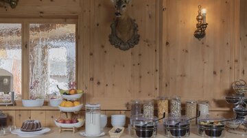 A cozy breakfast buffet with various fruits, yogurt, and cereals. The wooden walls and decorative elements create a warm atmosphere.