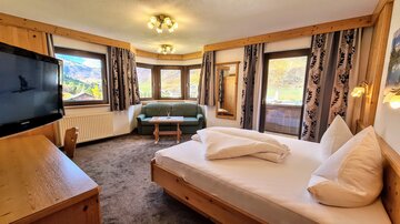 A cozy hotel room with a double bed and a living area. Large windows offer views of the surrounding landscape.