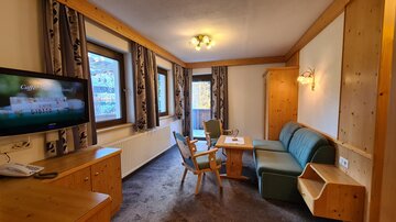A cozy living room with wooden details and modern furniture. There is a sofa, a table, and a television in front of a window.