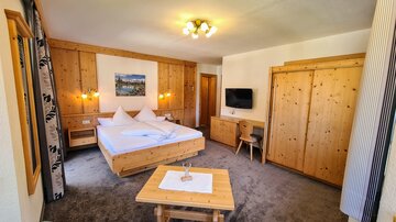A cozy room with wooden paneling and a large bed. The room has a flat-screen TV and a small table.