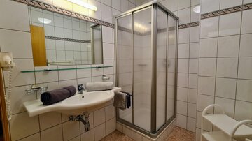 A clean bathroom with a shower cubicle and a sink. Towels are ready and the walls are tiled.