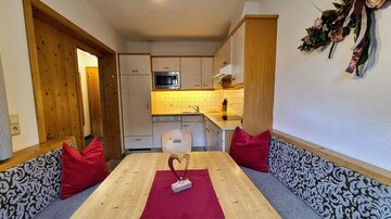 A cozy kitchen corner with a wooden table and red cushions. The modern kitchen is bright and well-equipped.