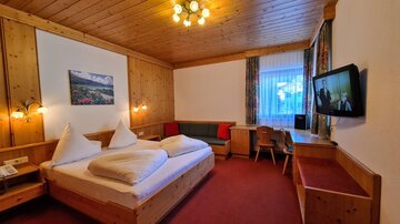 A cozy hotel room with wood paneling and a double bed. There is a television, a small table, and a window with curtains.