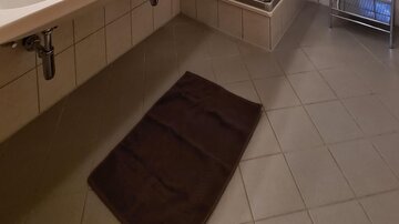 A modern bathroom with a shower and a large sink. The walls are tiled and the ceiling is made of wood.