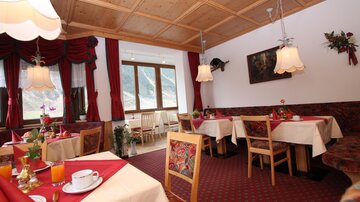 A cozy restaurant with tables decorated with red tablecloths and flowers. The wooden ceiling and warm colors create an inviting atmosphere.