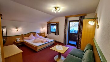 A cozy room with a double bed and a green sofa. Large windows provide plenty of daylight and a lovely view.