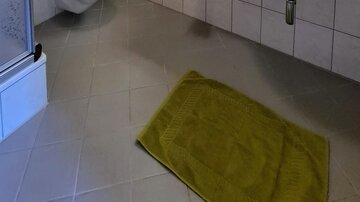 The bathroom is modernly furnished with white tiles and a wooden beam ceiling. It includes a shower, a sink, and green towels.