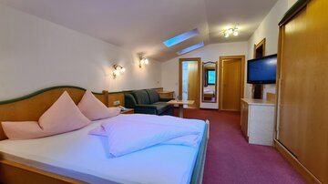 A cozy room with a double bed and pink cushions. There is also a seating area and a television.