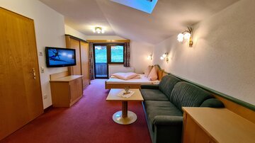 A cozy room with a sofa and a small table. There is a TV and access to a balcony with a beautiful view.