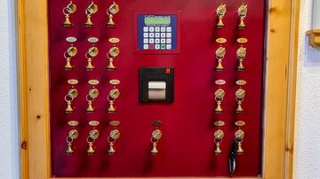 A wooden key rack with many keychains and a digital keypad. Below it is a shelf with brochures.