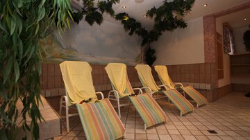 A relaxing room with four yellow loungers and colorful stripes. Green plants and a painting on the wall create a calm atmosphere.