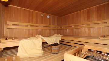 A cozy sauna with a wooden bench and a bucket. The walls are made of wood, and there is a clock on the wall.