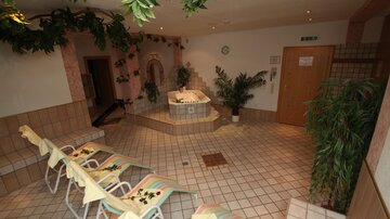 A relaxing wellness area with a jacuzzi and loungers. The atmosphere is pleasantly designed with plants and soft lighting.