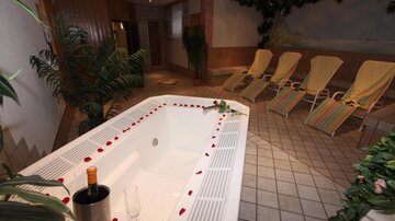 A relaxing wellness area with a hot tub and loungers. The surroundings are decorated with plants and there are rose petals in the water.