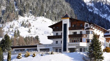 A cozy hotel in a snowy landscape. Surrounded by mountains and fir trees, it radiates winter tranquility.