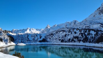 A beautiful frozen lake in a wintry mountain landscape. The high mountains are covered in snow and the sky is bright blue.