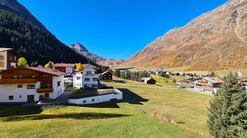 A picturesque mountain landscape with beautiful wooden chalets and green meadows in the foreground. The clear blue sky and the surrounding mountains create a relaxing atmosphere.