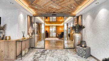 A stylish entrance with wooden ceilings and soft lighting. On the left stands an elegant console with decorations and on the right a carpet on the floor.