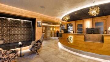 An elegant reception area with wooden-paneled walls and modern design. Cozy armchairs and a warmly lit counter create an inviting atmosphere.